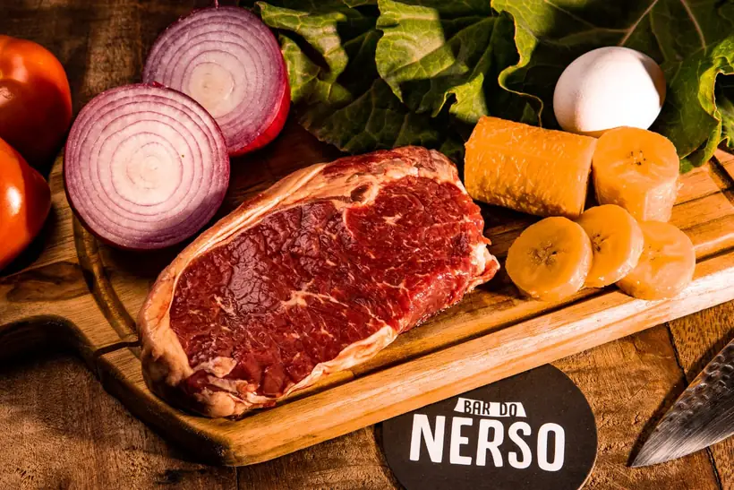 Peça bovina crua na tábua, ao lado de legumes frescos